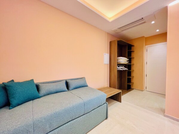 A modern room with a grey sofa, a wooden bench, a wardrobe, and a door. - YourHome - Lucrezia Suites (Sorrento)