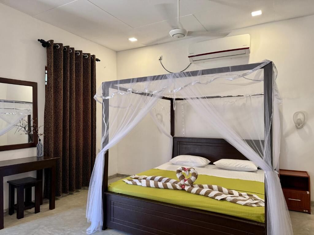 A room with a four-poster bed, a wooden nightstand, a desk with a chair, and a large mirror.