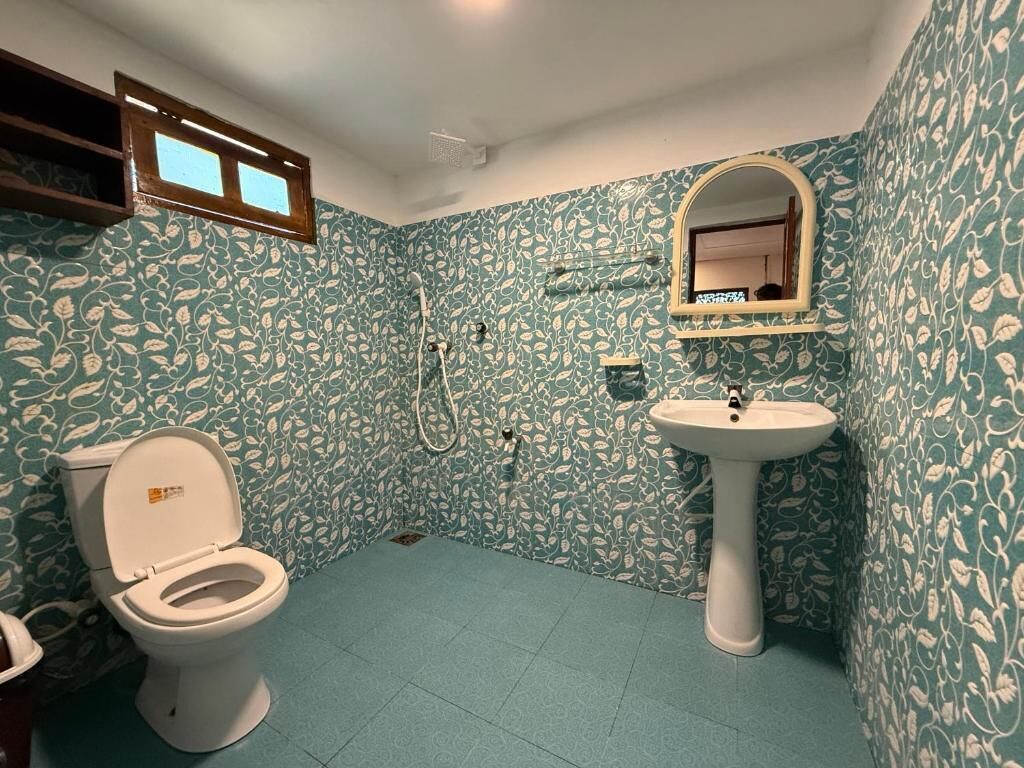 Ein Badezimmer mit Toilette, Waschbecken und Dusche. Die Wände sind mit einem Blattmuster versehen.