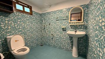 Ein Badezimmer mit Toilette, Waschbecken und Dusche. Die Wände sind mit einem Blattmuster versehen.