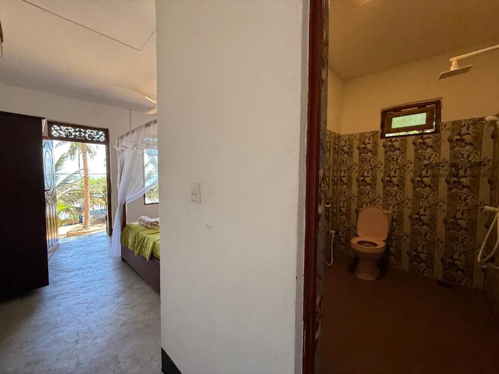 A room with a bed, a window with a view of palm trees, and a bathroom with a toilet and shower.