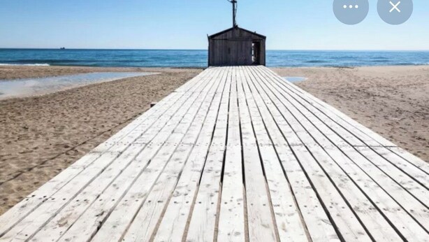 En träbrygga som leder fram till en liten byggnad på en strand.