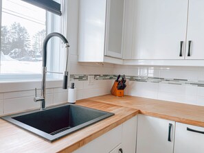 A modern kitchen with a black sink, white cabinets, and a wooden countertop. - Le Champery Tremblant 5 (Mont-Tremblant)