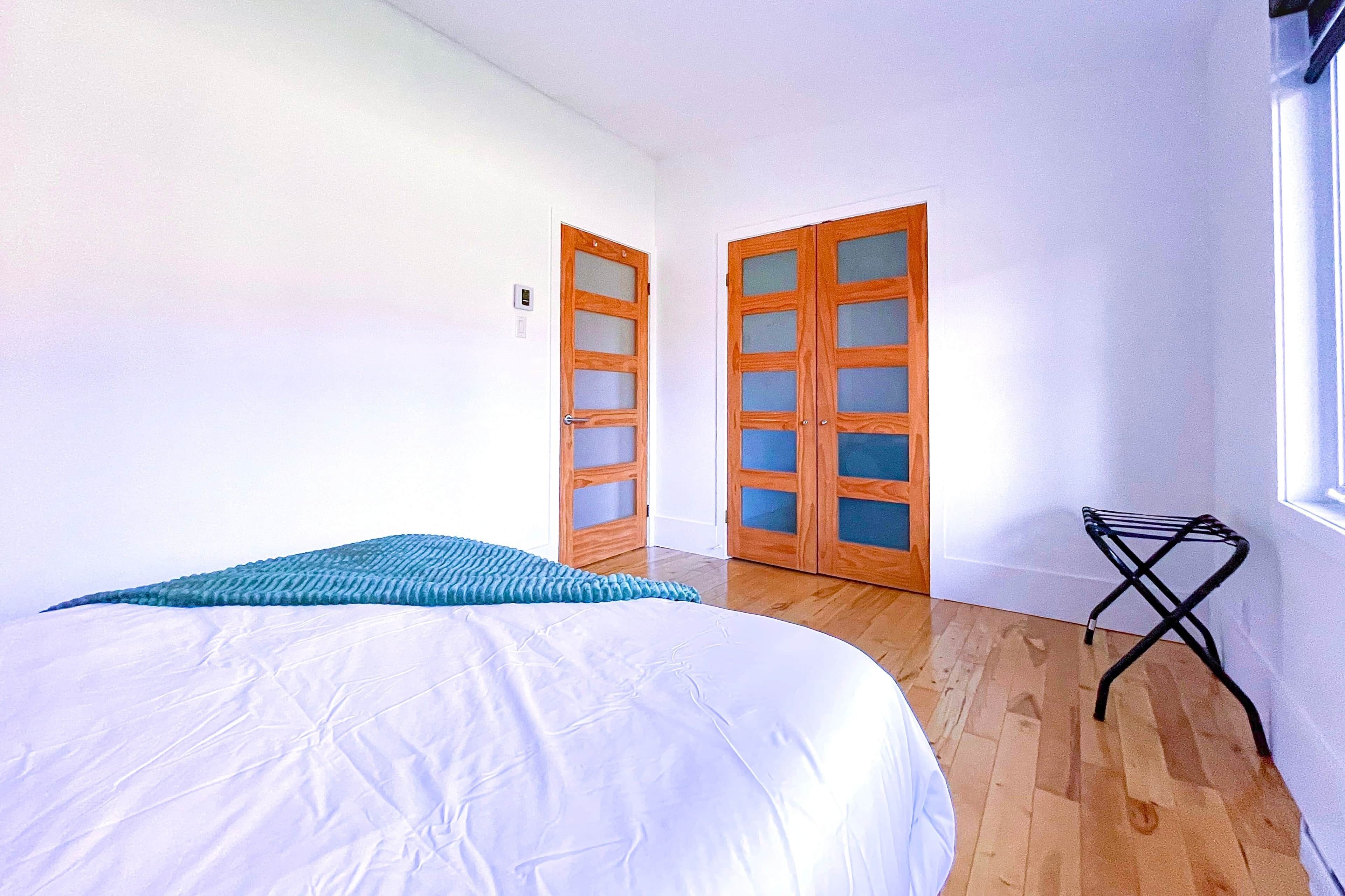 A room with a bed, two doors, a window, and a small table.