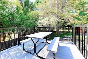 An outdoor patio with a picnic table and benches, surrounded by a metal railing and trees. - Le Champery Tremblant 4 (Mont-Tremblant)