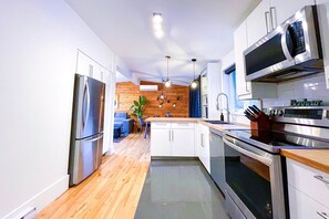 A modern kitchen with stainless steel appliances, wooden flooring, and white cabinetry. - Le Champery Tremblant 4 (Mont-Tremblant)