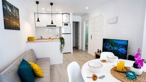 A modern kitchen with white cabinets, a dining area with a white table, and a living room with a television. - Sun and Beach in La Mata (Torrevieja)