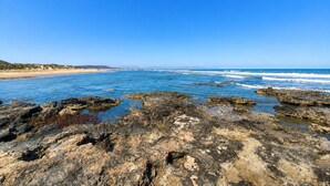 A rocky shoreline with clear blue water and a distant beach. - Sun and Beach in La Mata (Torrevieja)