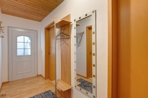Un couloir avec une porte en bois, un miroir avec un cadre en bois et un banc.