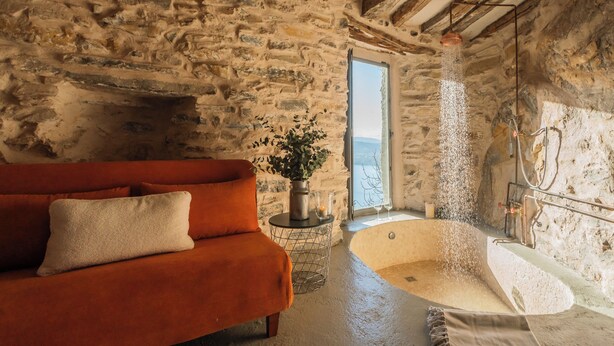 Una habitación de paredes de piedra con una bañera grande, un sofá rojo y una planta en maceta.