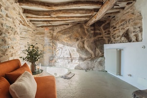 Un interior rústico de piedra con un sofá naranja moderno, una mesita con una vela y un radiador.