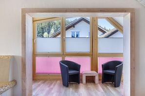 A room with a wooden-framed window, two black chairs, a small wooden stool, and a wicker chair. - Apartment 'Af' with Shared Garden, Balcony and Wi-Fi (Bonndorf im Schwarzwald)