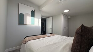 A bedroom with a bed, a framed artwork on the wall, and a door leading to another room. - Serene Escape: 1 Bed 1 Bath Private Basement Suite| 12 mins to Spruce Meadows (Calgary)