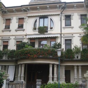 A building with a classical architectural style, featuring a central entrance with columns, multiple windows with shutters, and a balcony with plants. - Stylish Penthouse in Venice Lido with Amazing views, central and close to beach! (Lido)