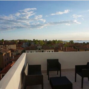 A balcony with four dark-colored chairs and a small table, overlooking a coastal town with buildings and a body of water in the distance. - Stylish Penthouse in Venice Lido with Amazing views, central and close to beach! (Lido)