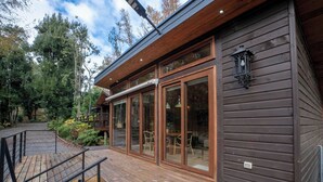 A wooden cabin with large sliding glass doors, a deck, and a lantern on the exterior wall. - Rincón Nativo 3D y Piscina (Pucón)