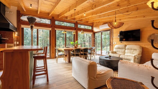 A spacious wooden interior with a dining area, a sofa, and a TV mounted on the wall. - Rincón Nativo 3D y Piscina (Pucón)