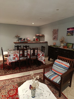 Un comedor con una mesa dispuesta para seis personas, rodeada de sillas. En primer plano, una mesa pequeña con un jarrón de flores.