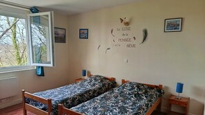 Une pièce avec deux lits en bois, une fenêtre et un mur décoré de plumes et orné d’une phrase en français.