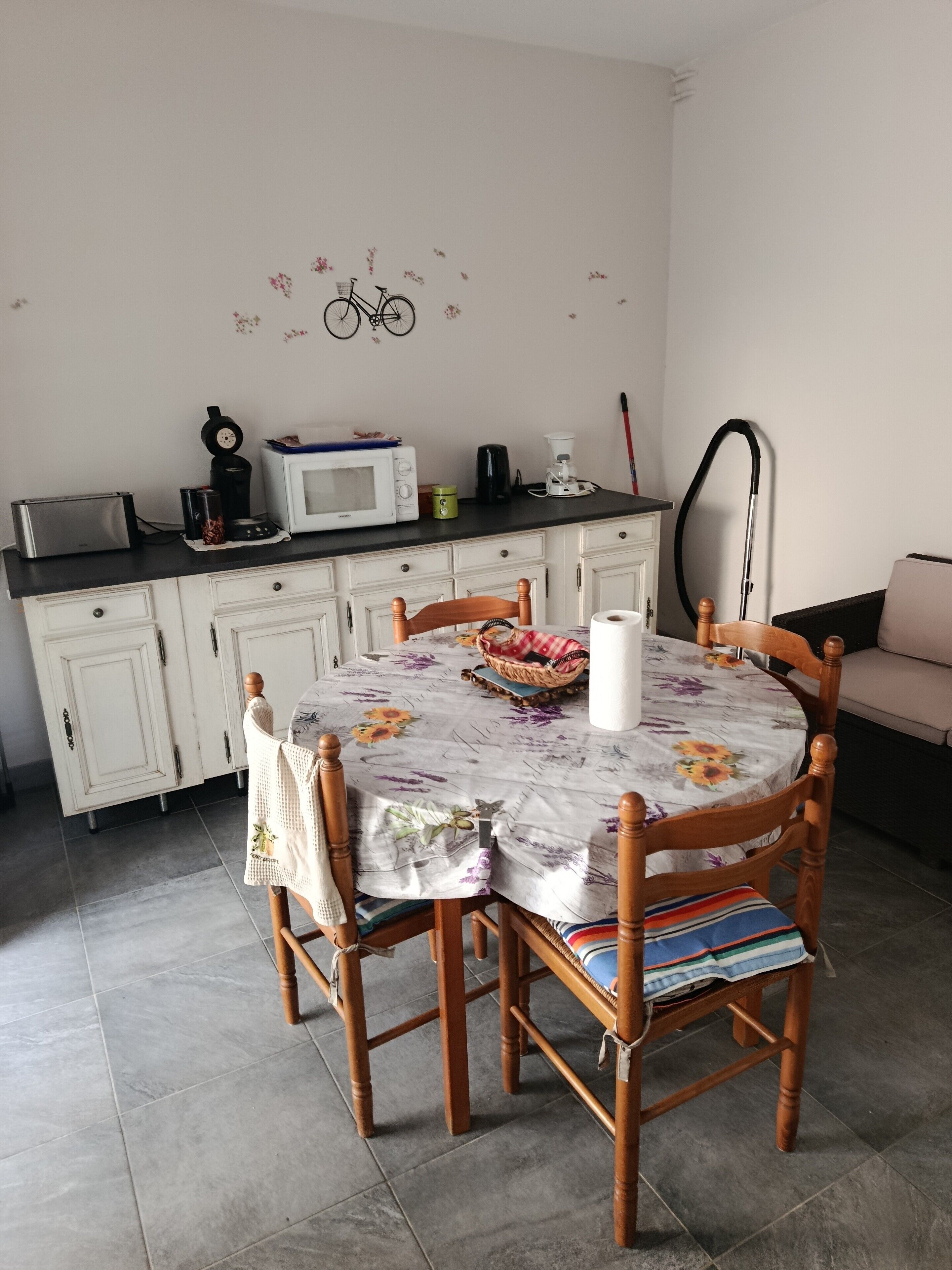 Un comedor con una mesa redonda, sillas, un microondas, un tostador y una aspiradora.