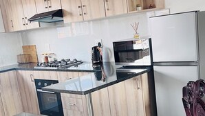Ett modernt kök med träskåp, ett matbord i glas, vitvaror i rostfritt stål och ett klinkergolv.