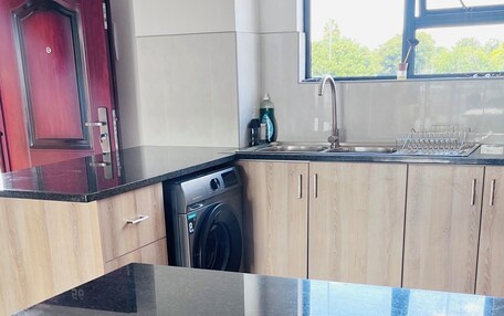 A kitchen with a black countertop, a washing machine, a red door, and a window with a view of greenery.