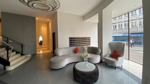 Eine moderne Lobby mit einer gebogenen grauen Couch, einem runden Hocker und einem großen Fenster mit Blick auf die Straße.