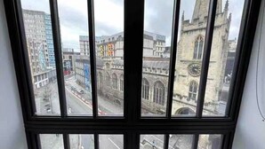Blick durch ein Fenster auf eine Stadtlandschaft mit modernen Gebäuden und einem historischen Glockenturm.