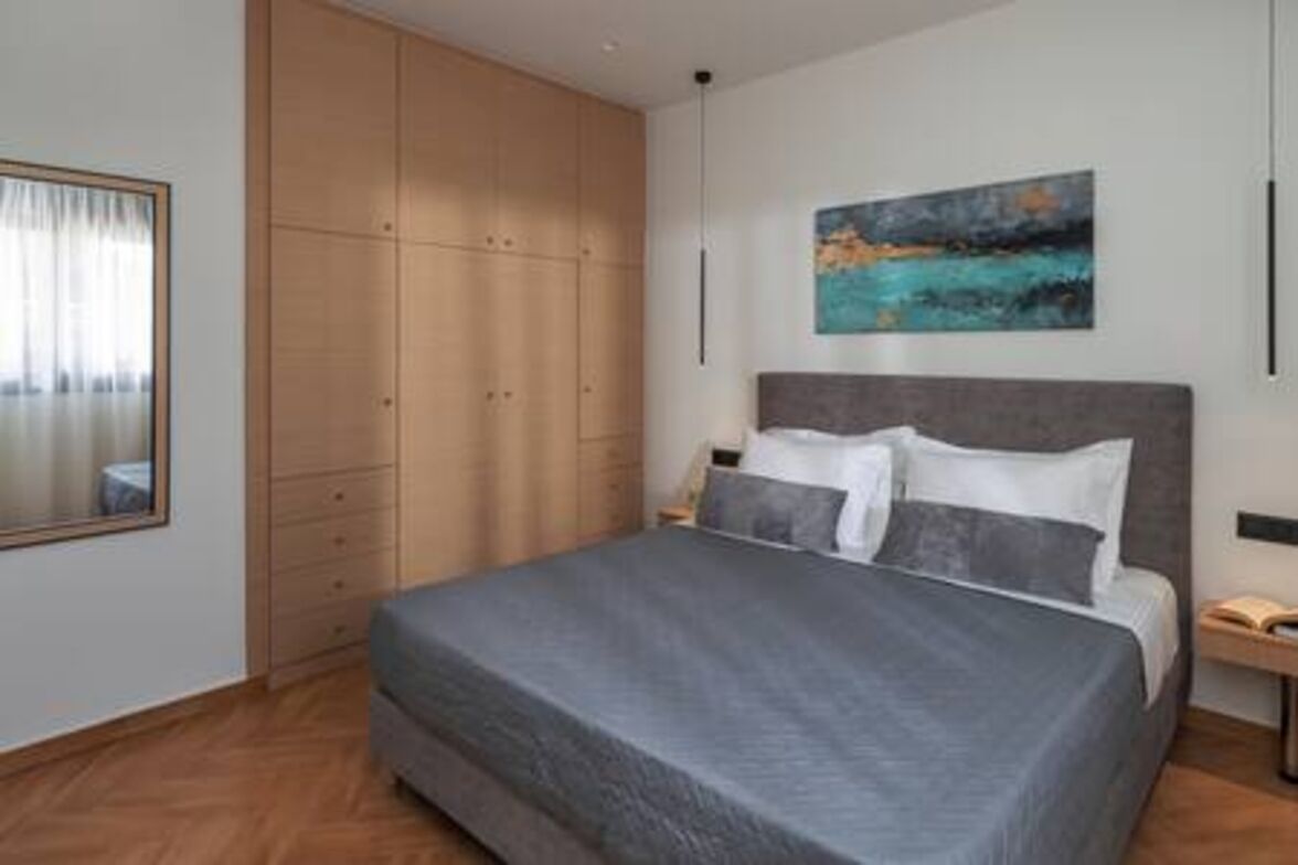 A bedroom with a bed, a wardrobe, a painting, and a bedside table.