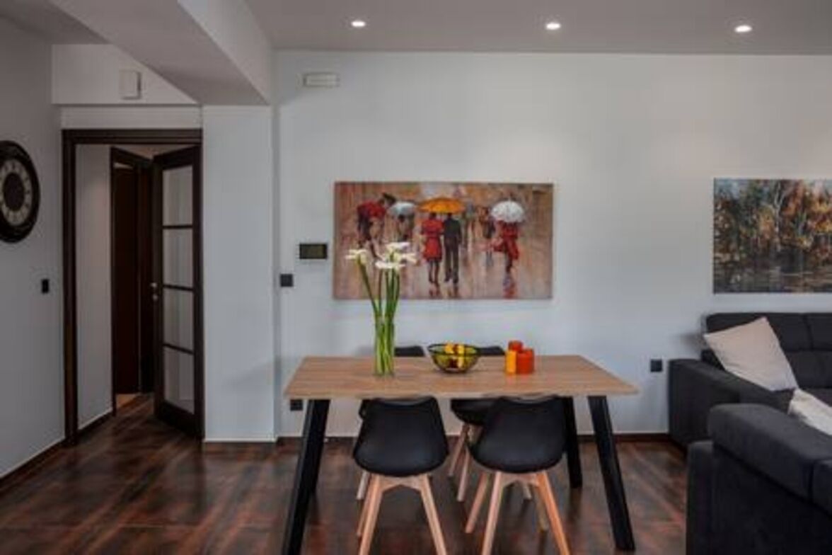 Un salon moderne avec un coin repas, comprenant une table en bois, des chaises noires, un canapé noir et deux tableaux accrochés au mur.