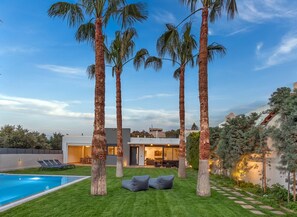 Une maison moderne dotée d’une piscine, de palmiers et d’une pelouse bien entretenue.