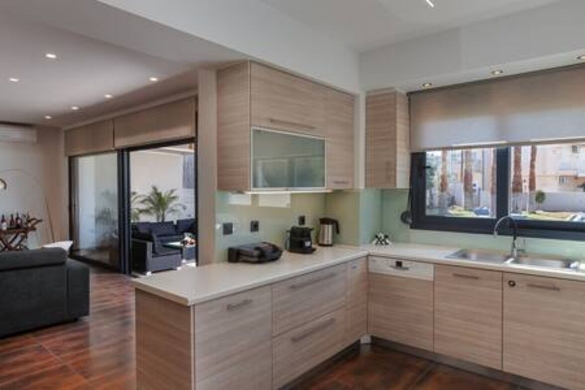 A modern kitchen with light wood cabinets, a large window, and a built-in TV.