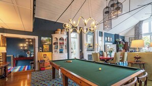 A pool table in a room with a patterned carpet, a chandelier, and a dining area with chairs and a table. - The Church House Spacious Heritage Escape for Two (North Hobart)