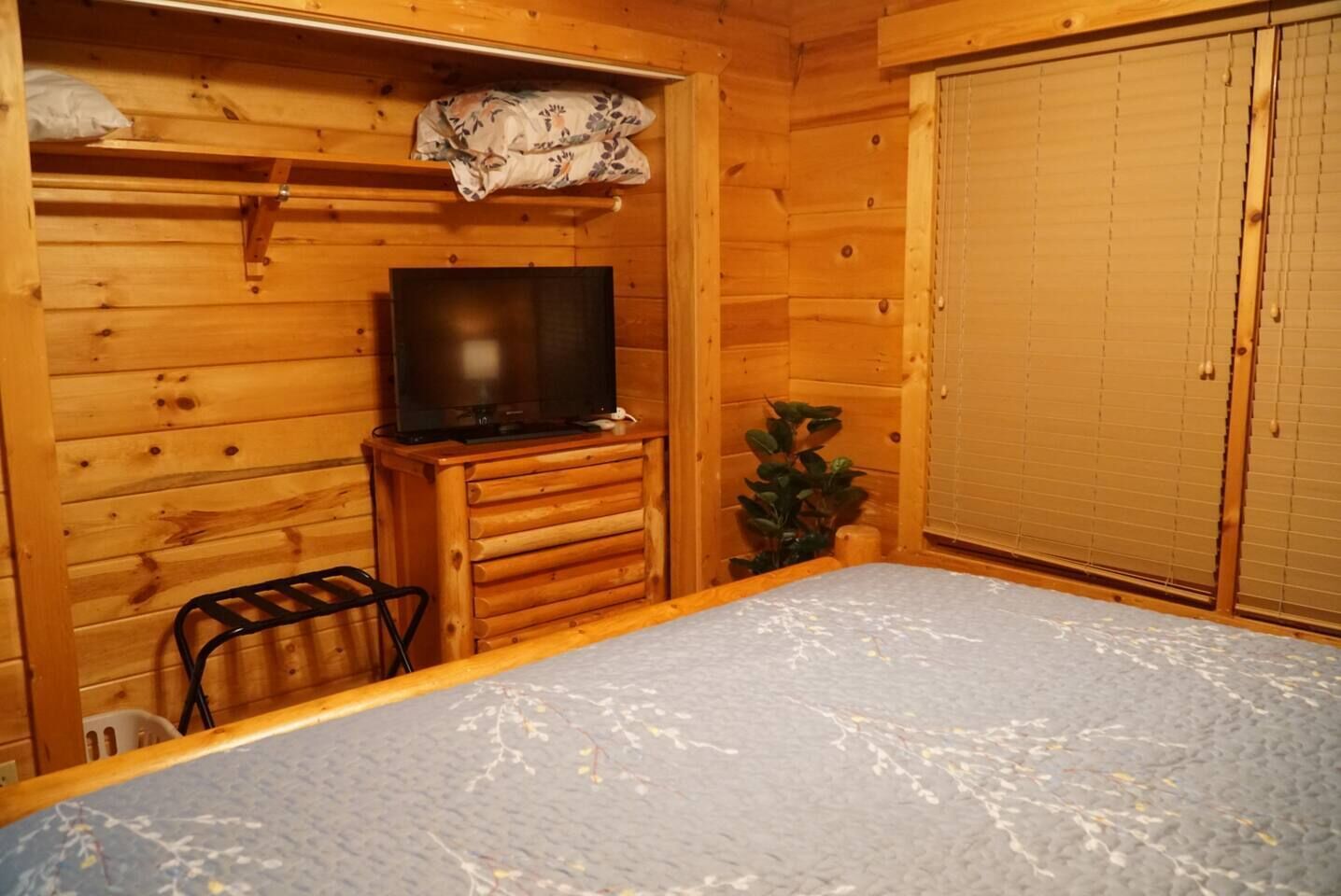 A wooden cabin room with a bed, a television on a wooden stand, and a wardrobe.