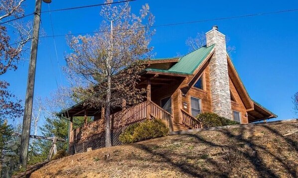 A log cabin with a stone chimney, wooden deck, and a hillside location. - Discover the perfect getaway at Square Bear in Sevierville, TN, where luxury and (Sevierville)