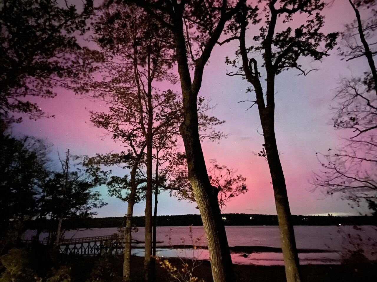 Ein Nachtblick auf eine Brücke über dem Wasser, mit silhouettierten Bäumen vor einem rosa Himmel.
