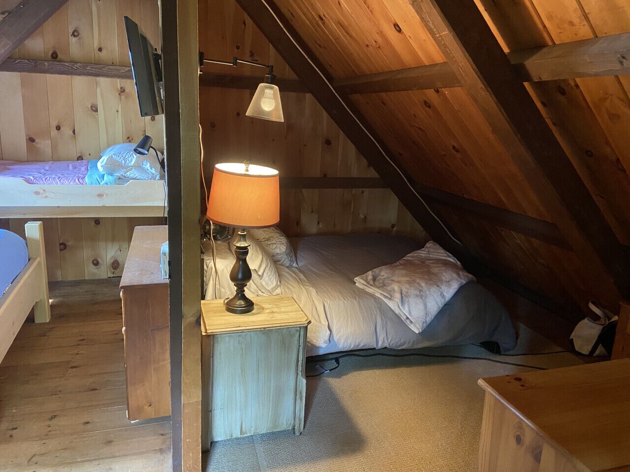 A small, cozy attic bedroom with a single bed, a nightstand with a lamp, and a wooden desk.