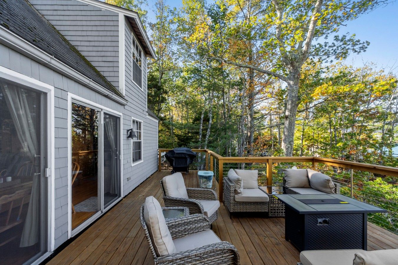 A deck with outdoor furniture, a grill, and a view of trees.