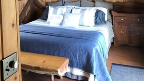 Ein Schlafzimmer einer Holzhütte mit einem Bett, einem Nachttisch, einer Bank und einem Deckenventilator.