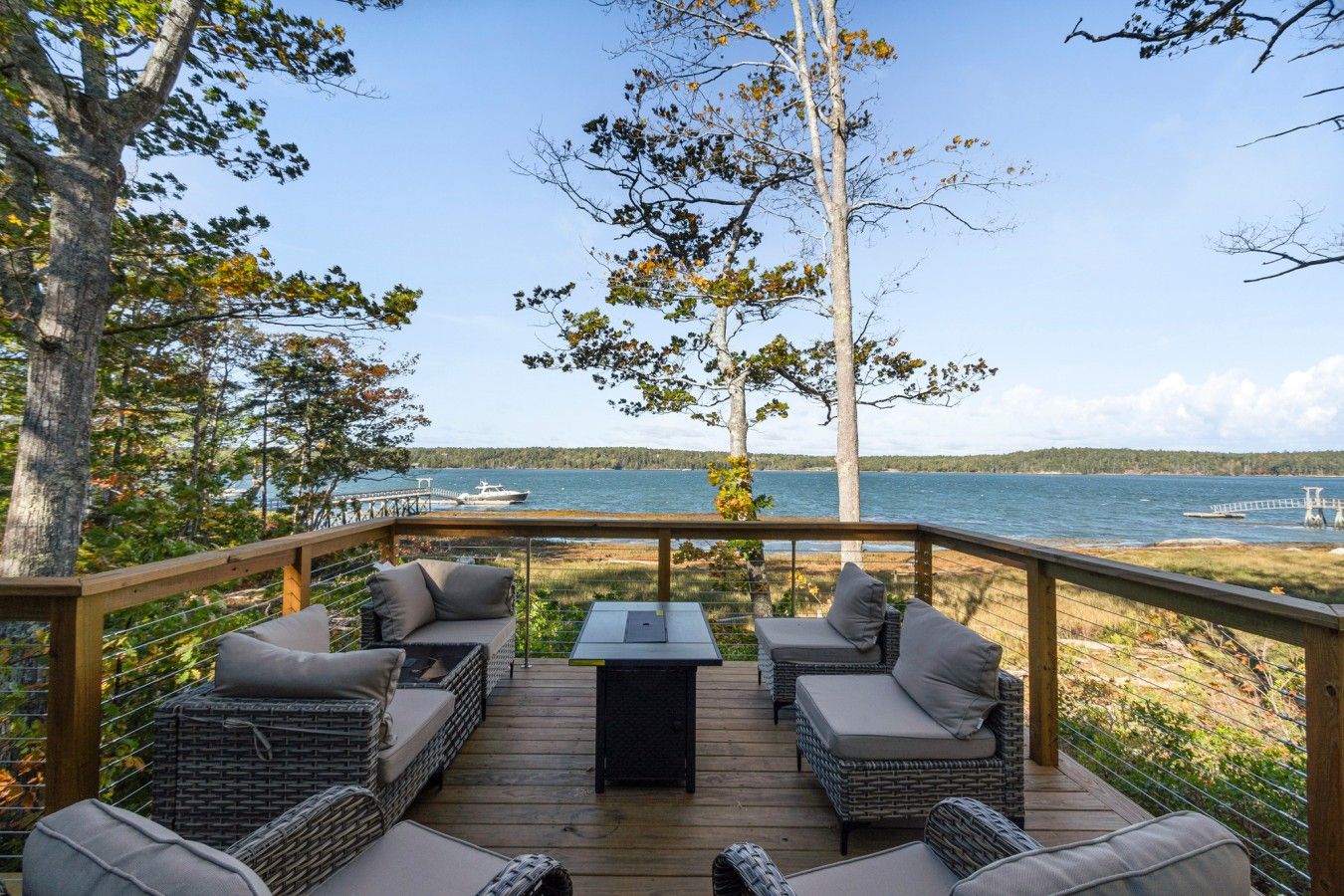 A deck with wicker furniture and a table, overlooking a body of water and a dock.