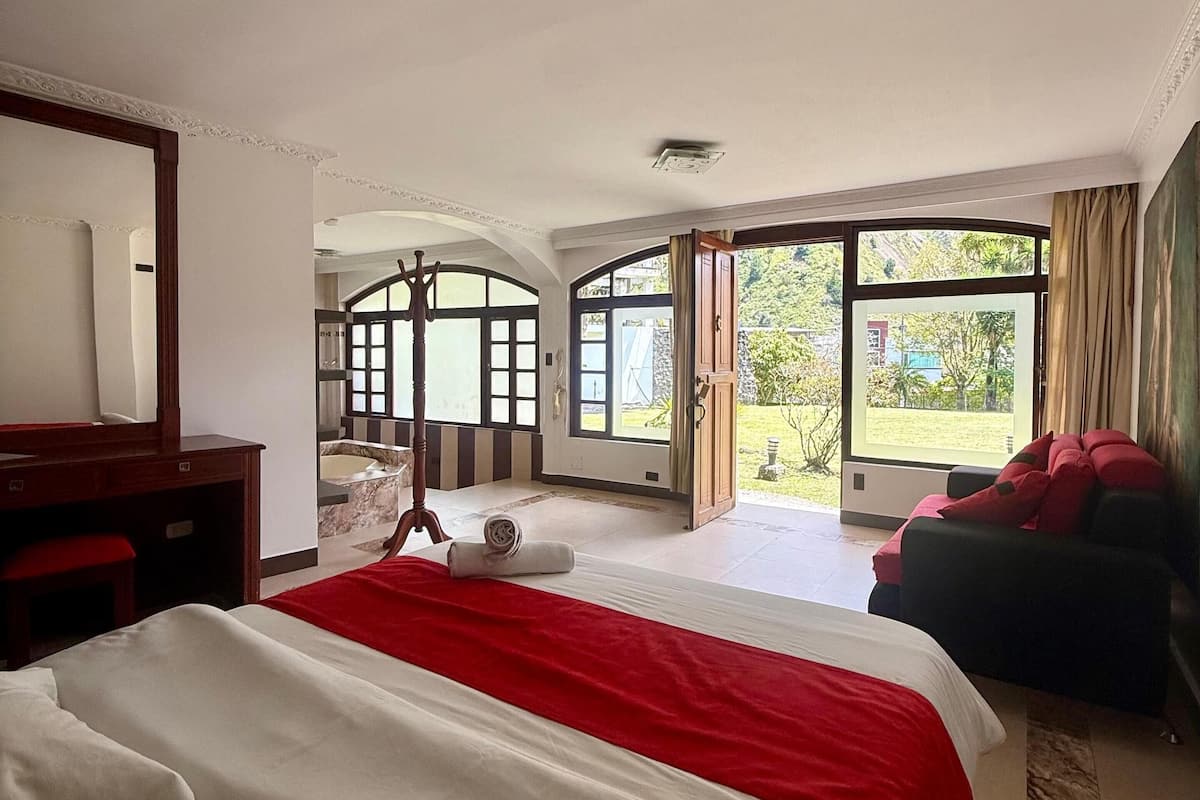 Une chambre d’hôtel avec un grand lit, un bureau, une chaise et une vue sur l’extérieur grâce à de grandes fenêtres.