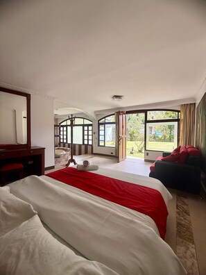 Une chambre d’hôtel avec un grand lit, un bureau, une chaise et une vue sur l’extérieur grâce à de grandes fenêtres.
