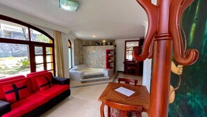 Ein Zimmer mit einem roten Sofa, einem Holztisch, einer Steinwand und Blick ins Freie.