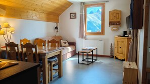 A cozy room with a wooden ceiling, a sofa, a dining table with chairs, a small cabinet, and a window with a mountain view. - Comfortable 6-person apartment Saint Jean d'Arves les Sybelles 3* rated (Saint-Jean-d'Arves)