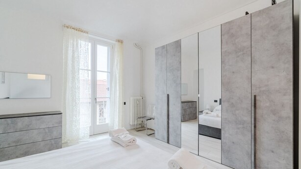 A modern bedroom with a large wardrobe, a bed, a radiator, and a window with curtains. - GuestHost - A bright and welcoming 50 square meters apartment, perfect for four people, located on the third floor of a building without an elevator.The property is located in a very quiet area and is close to San Giovanni Bosco Hospital. Thanks to publi (Turin)