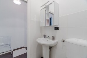 A bathroom with a white sink, a mirror, a toilet, and a chair. - GuestHost - A bright and welcoming 50 square meters apartment, perfect for four people, located on the third floor of a building without an elevator.The property is located in a very quiet area and is close to San Giovanni Bosco Hospital. Thanks to publi (Turin)