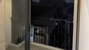 A bedroom with a bed, a sliding glass door leading to a balcony, and a view of buildings outside. - ERA Trung Liet SIGNATURE (Hanoi)