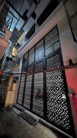 Fachada de edifício com um gradeado preto decorativo, aparelhos de ar condicionado e uma escadaria visível que dá acesso a um andar superior.