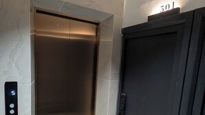 An elevator with a digital display, a door with a number plate, and a wall-mounted emergency light. - ERA Trung Liet SIGNATURE (Hanoi)