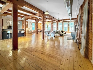 A spacious room with wooden floors, exposed beams, and large windows.